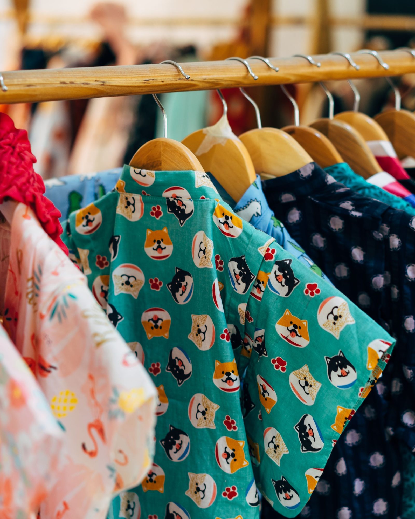 Portant d’une friperie : polos, chemises à motifs et t-shirts d’occasion sur des cintres en bois.